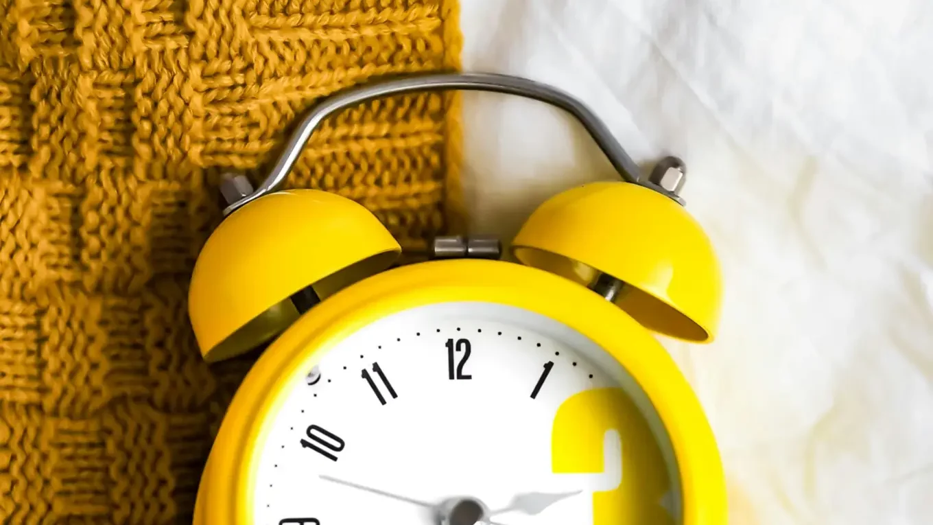 Réveil jaune posé sur une couverture, utilisé pour illustrer la gestion du temps avec la méthode Pomodoro